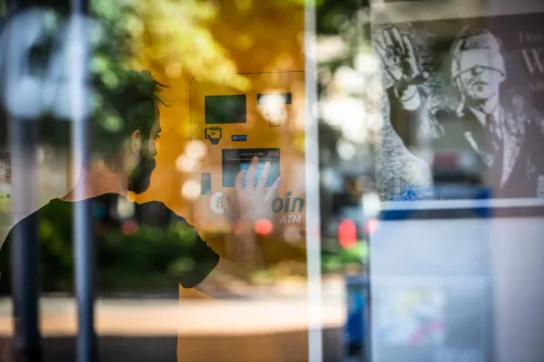 رجل يستخدم ماكينة صراف آلي للعملات الرقمية، مع وجود صورة خلفية توضح تفاصيل العملات الرقمية. تعكس الصورة تزايد الاهتمام بالبيتكوين والإيثر.