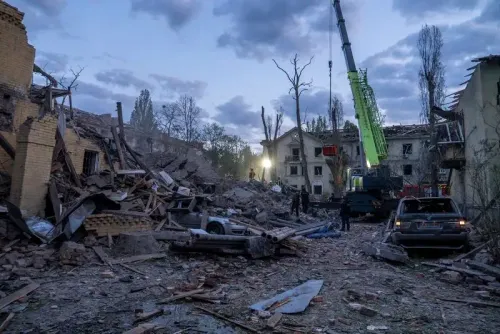 تظهر الصورة مشهدًا مدمرًا في منطقة حضرية، حيث تهدمت المباني بفعل القصف، مع وجود عمال إنقاذ ومركبات في الموقع.