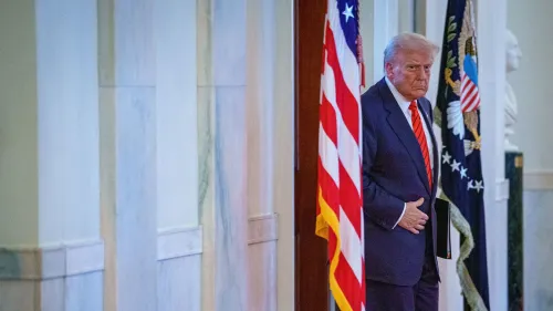 ترامب يدخل غرفة مع العلم الأمريكي خلفه، معبرًا عن التحدي والنفوذ في سياق إدارته الجديدة.