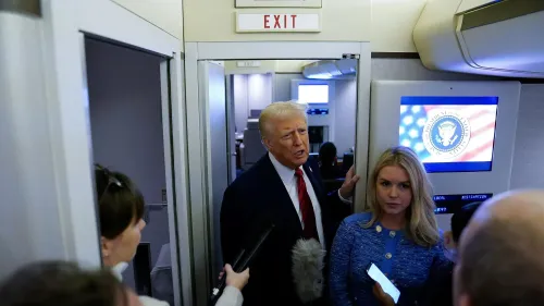 دونالد ترامب يتحدث مع الصحفيين في ممر الطائرة الرئاسية، مع وجود شاشة تعرض شعار الحكومة الأمريكية خلفه.