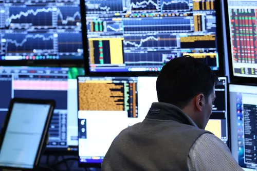شخص يعمل في غرفة تداول، محاط بشاشات تعرض بيانات سوق الأسهم والرسوم البيانية، مما يعكس تقلبات السوق وأداء الأسهم.
