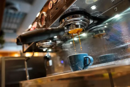 تدفق قهوة الإسبريسو من ماكينة تحضير القهوة إلى فنجان زجاجي، مما يعكس تأثير ارتفاع أسعار البن على محلات القهوة.