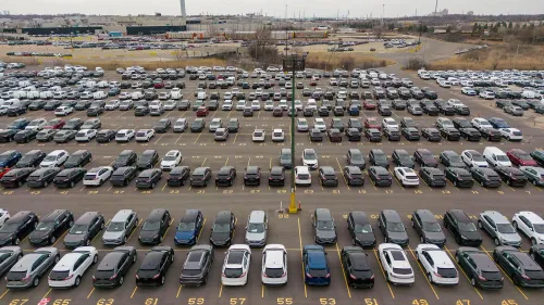 صورة لصفوف من السيارات المتوقفة في موقف سيارات واسع، تُظهر تأثير التوترات التجارية على صناعة السيارات.