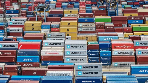 صورة لميناء مزدحم بحاويات شحن ملونة، تعكس تأثير الحرب التجارية بين الولايات المتحدة والصين على التجارة العالمية.