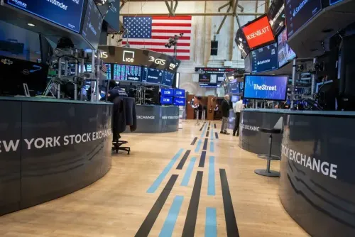 صورة لقاعة بورصة نيويورك، تُظهر شاشات عرض الأسعار والرسوم البيانية، مع العلم الأمريكي في الخلفية، تعكس حالة الأسواق المالية.