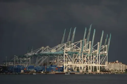 صورة لميناء يحتوي على رافعات ضخمة ومعدات تحميل، مع حاويات شحن ملونة، تعكس تأثير السياسة التجارية على الأسواق العالمية.