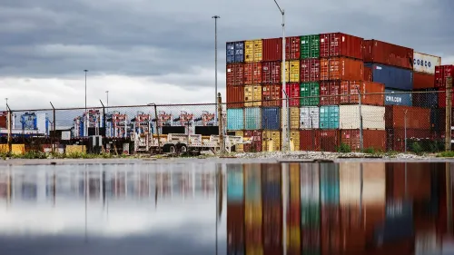 صورة لمستودع يحتوي على حاويات شحن ملونة مرتبة بشكل عشوائي، تعكس تأثير التوترات التجارية العالمية على الاقتصاد.