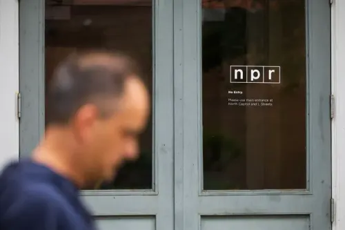 شخص يسير بالقرب من مدخل محطة الإذاعة الوطنية العامة (NPR) حيث تظهر لافتة "لا دخول" على الباب، مما يعكس التحديات المالية التي تواجهها الشبكة.