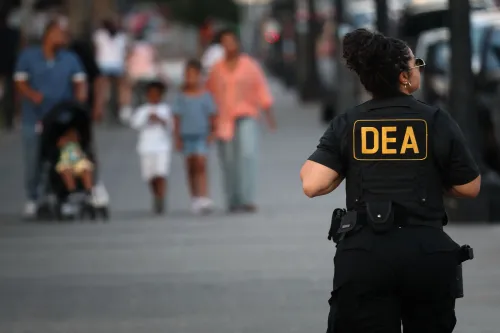 ضابط من DEA يرتدي زيًا رسميًا ويشرف على منطقة مزدحمة في واشنطن العاصمة، حيث يسير الناس في الخلفية.