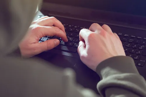 أيدٍ ترتدي سترة رمادية تعمل على لوحة مفاتيح حاسوب محمول، مما يعكس نشاطًا في مجال الأمن السيبراني وتهديدات برمجيات الفدية.