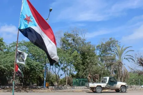 علم المجلس الانتقالي الجنوبي يرفرف في عدن، مع وجود سيارة عسكرية في الخلفية، مما يعكس التوترات السياسية والأمنية في اليمن.