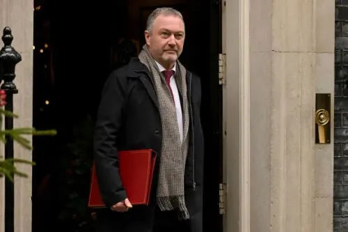رجل يرتدي معطفًا داكنًا وشالًا، يحمل ملفًا أحمر، يخرج من مبنى حكومي، في سياق تحقيق حول التدخل الأجنبي في السياسة البريطانية.