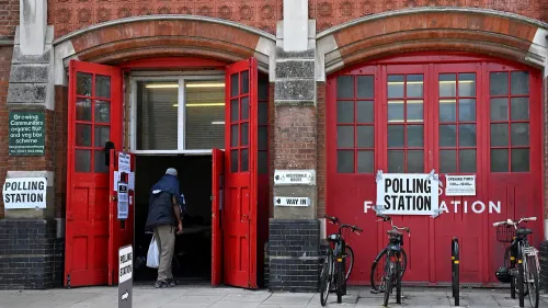 مدخل مركز اقتراع في المملكة المتحدة، مع لافتات توضح أوقات العمل، ودراجة بجانب الباب، مما يعكس جهود تعزيز المشاركة الديمقراطية.