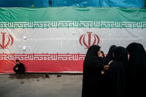 نساء يرتدين الحجاب الأسود يتحدثن معًا أمام علم إيران الكبير، في سياق التوترات السياسية المرتبطة بأنشطة الاستخبارات الإيرانية.