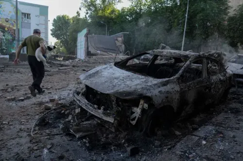 رجل يحمل كلبًا يسير بجانب سيارة محترقة وسط أنقاض مبنى مدمر، مما يعكس آثار القصف المستمر في أوكرانيا.