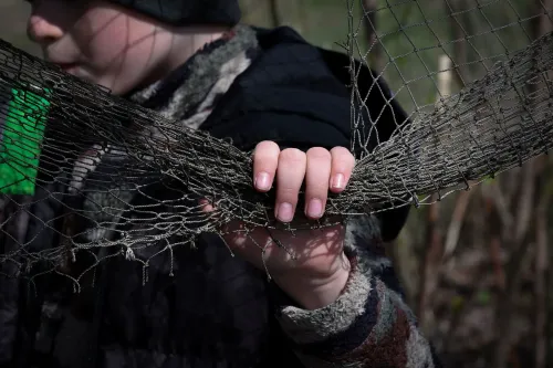 يد تحمل شبكة صيد قديمة، بينما يظهر في الخلفية طفل يرتدي ملابس داكنة، تعكس مشهد الحياة تحت تأثير الحرب في أوكرانيا.