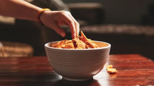 يد تظهر يد شخص تأخذ وجبة خفيفة من وعاء مليء برقائق snack، مما يعكس شغف الأطعمة فائقة المعالجة وتأثيرها على النظام الغذائي.