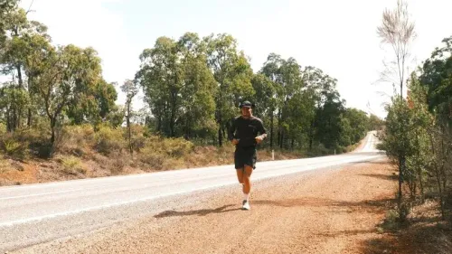 عداء يتدرب على طريق ريفي في أستراليا، محاط بالأشجار، أثناء سعيه لتحطيم الرقم القياسي للجري عبر البلاد.