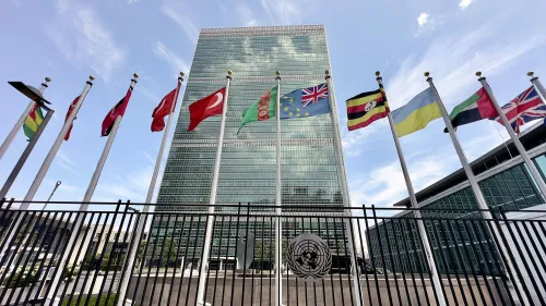 مبنى الأمم المتحدة محاط بأعلام دول متعددة، مع سماء زرقاء وصافية، مما يعكس التنوع الدولي في مواجهة الأزمات الإنسانية.