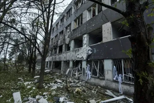 مبنى مدمر في منطقة قريبة من خط المواجهة، مع نوافذ مكسورة و debris في الحديقة المحيطة، مما يعكس آثار الصراع المستمر.