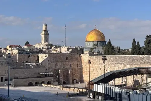 مشهد لمدينة القدس القديمة يظهر قبة الصخرة والمآذن، مع شوارع فارغة ومحلات مغلقة، مما يعكس تأثير الأوضاع السياسية على الحياة اليومية.