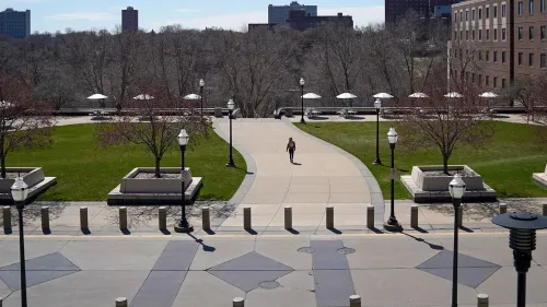 امرأة تسير بمفردها في حرم جامعة مينيسوتا، حيث تظهر الأشجار والأضواء في الخلفية، مما يعكس أجواء الدراسة والهدوء.