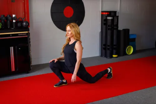 امرأة تؤدي تمارين الإطالة لكاحليها في صالة رياضية، مع معدات رياضية خلفها، تبرز أهمية حركة الكاحل في تحسين الأداء البدني.