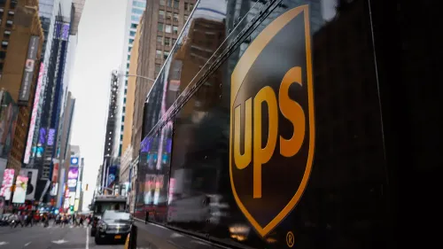شعار شركة UPS يظهر على شاحنة في مدينة مزدحمة، مع خلفية من المباني العالية، مما يعكس التحديات التي تواجهها الشركة في السوق.