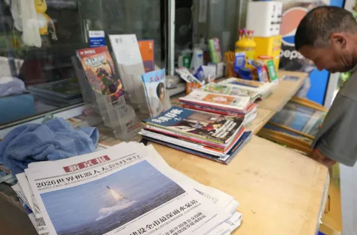 رجل صيني في كشك صحف يعرض صحفاً ومجلات تتناول موضوعات نووية وعسكرية، تعكس النقاشات الأمريكية-الصينية حول الزيارات المتبادلة للمواقع النووية.