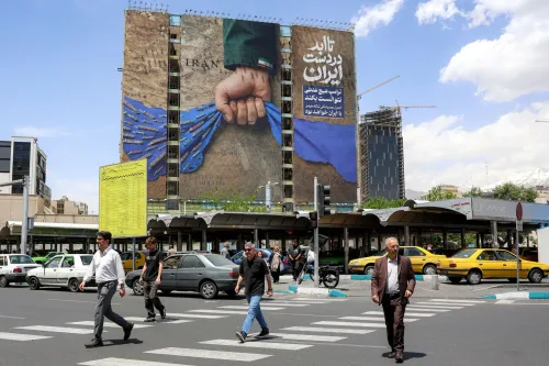 لوحة جدارية في طهران تظهر يدًا تمسك بشريط أزرق، مع نصوص تدعو إلى الوحدة الإيرانية، بينما يمر الناس في الشارع.