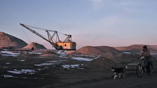 مشهد لآلة حفر كبيرة تعمل في منطقة تعدين، بينما يمر شخص بدراجة مع كلبه، مما يعكس أهمية الموارد الطبيعية في أوكرانيا.