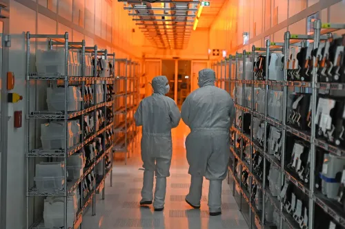 ممر في مصنع نيكسبيريا حيث يرتدي العاملون ملابس واقية، مع رفوف تحتوي على مكونات إلكترونية ضرورية لصناعة السيارات.