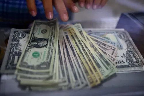 أوراق نقدية من الدولار الأمريكي مع يد تضعها، تعكس التحولات في التجارة الدولية نحو استخدام العملات المحلية بدلاً من الدولار.