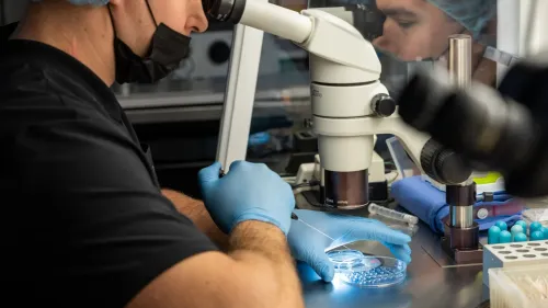 تقني يعمل في مختبر لتقنيات الإخصاب في المختبر، مركزًا على عينة تحت المجهر، وسط معدات طبية متطورة.