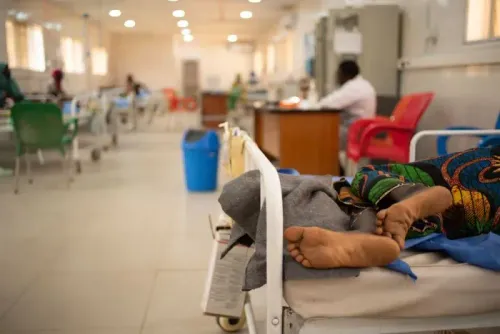 امرأة مريضة ملقاة على سرير في مستشفى، تعكس تأثير الملاريا في جمهورية الكونغو الديمقراطية، حيث تعاني الأسر من نقص في العلاج والرعاية.