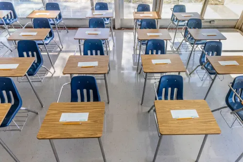 فصول دراسية فارغة تحتوي على طاولات وكراسي زرقاء، مع أوراق اختبار موضوعة على الطاولات، تعكس تراجع مستويات التعليم.