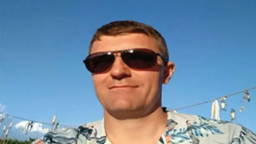 رجل يرتدي نظارات شمسية وقميص مزخرف، يظهر في صورة شخصية تحت سماء زرقاء، وهو متهم بقيادة عصابة جرائم إلكترونية عالمية.