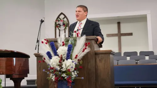 واعظ أمريكي يلقي خطبة في كنيسة، مع زهور ملونة وزينة خلفه، في سياق حديث عن عملية إنقاذه من الاختطاف في جنوب أفريقيا.
