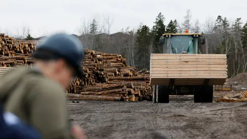 شاحنة تحميل تحمل الخشب اللين في موقع بناء، مع كومة من الأخشاب في الخلفية، تعكس النزاع التجاري بين الولايات المتحدة وكندا.