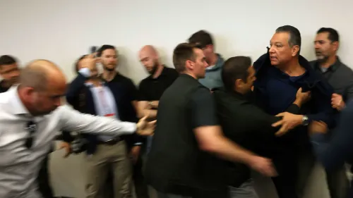 مشهد من مؤتمر صحفي في لوس أنجلوس يظهر السيناتور أليكس باديلا محاطًا بالمسؤولين بينما يتم إخراجه بالقوة.