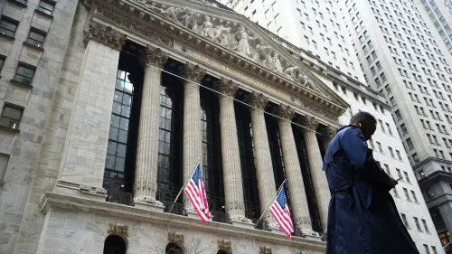 واجهة بورصة نيويورك مع أعلام أمريكية ورجل يرتدي معطفًا، تعكس حالة السوق المتقلبة والهبوط الحاد في الأسهم.