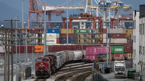 قطار شحن يمر عبر محطة حاويات، مع ظهور حاويات ملونة من شركات مثل \"Evergreen\" و\"Maersk\" في الخلفية، مما يعكس حركة التجارة.