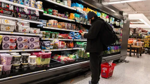 شخص يتسوق في متجر، يركز على اختيار المواد الغذائية من الرفوف، مع تواجد مجموعة متنوعة من المنتجات.