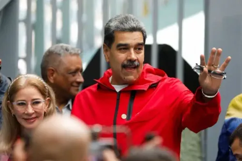 مادورو، الرئيس الفنزويلي، يلوح بيده خلال حدث عام، مرتديًا سترة حمراء، مع وجود أشخاص آخرين في الخلفية.