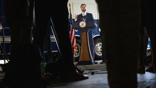 نائب الرئيس جيه دي فانس يتحدث من منصة خلال مؤتمر صحفي في لوس أنجلوس، محاطًا بالصحفيين، مع العلم الأمريكي خلفه.