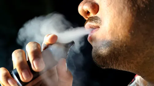 رجل يدخن السيجارة الإلكترونية، حيث يخرج بخار من فمه، مما يعكس المخاطر الصحية المحتملة المرتبطة بالتدخين الإلكتروني.