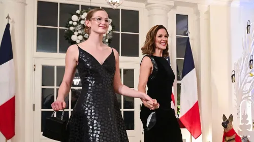 في الصورة، فيوليت أفليك تسير مع والدتها جينيفر غارنر، وكلاهما ترتديان فساتين أنيقة. الخلفية تتضمن زينة احتفالية.