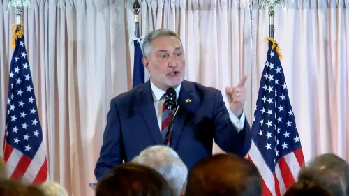 جون ريد، مرشح نائب الحاكم في فيرجينيا، يتحدث أمام جمهور، مع أعلام أمريكية خلفه، في سياق الجدل السياسي حول حساب متنازع عليه.