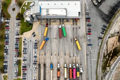 صورة جوية لمركز توزيع يحتوي على شاحنات ملونة متوقفة في صفوف، مع وجود سيارات في موقف السيارات المجاور.