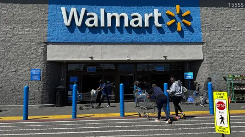 مدخل متجر وول مارت، حيث يتسوق الزبائن مع عربات التسوق، مع وجود لافتة تحذيرية على الرصيف. تعكس الصورة تأثير الرسوم الجمركية على الأسعار.